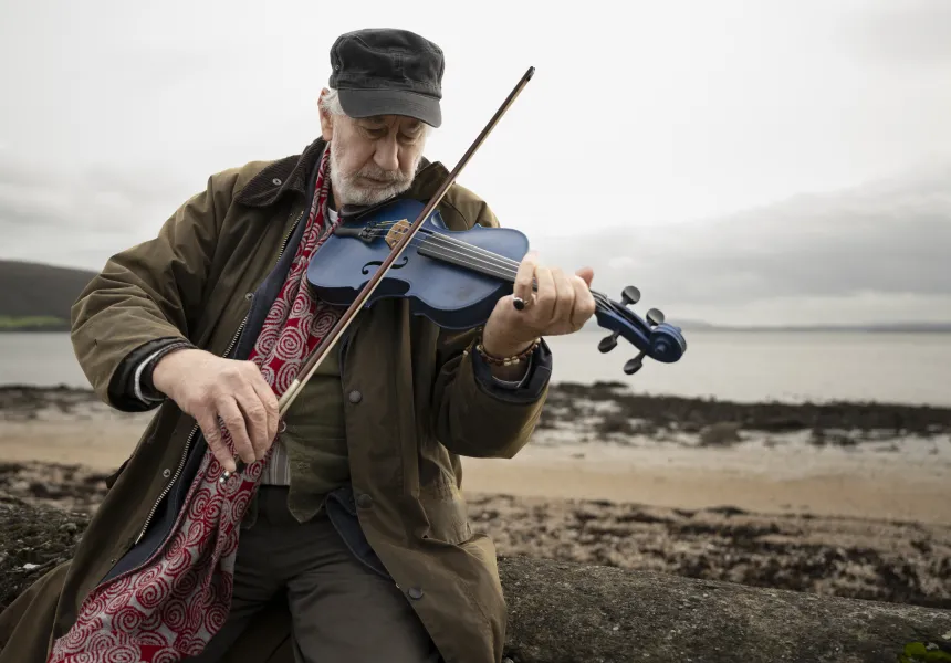 Fidil Ghorm still - Barry Mcgovern playing a blue violin on the beach