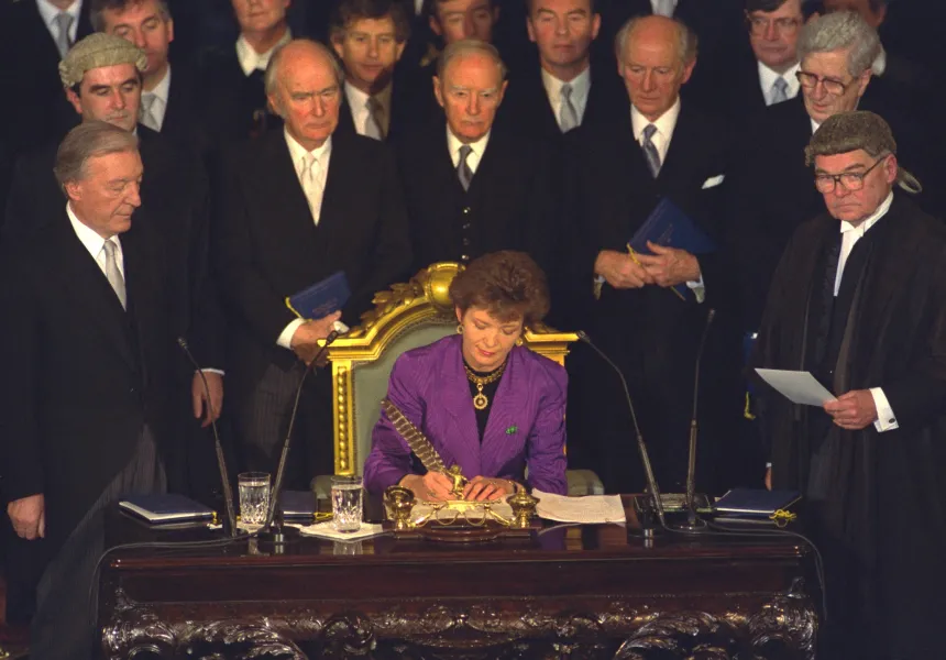 Mary Robinson signing papers in front of a group of politicians