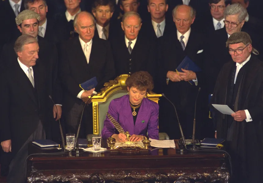 Mary Robinson signing papers in front of a group of politicians